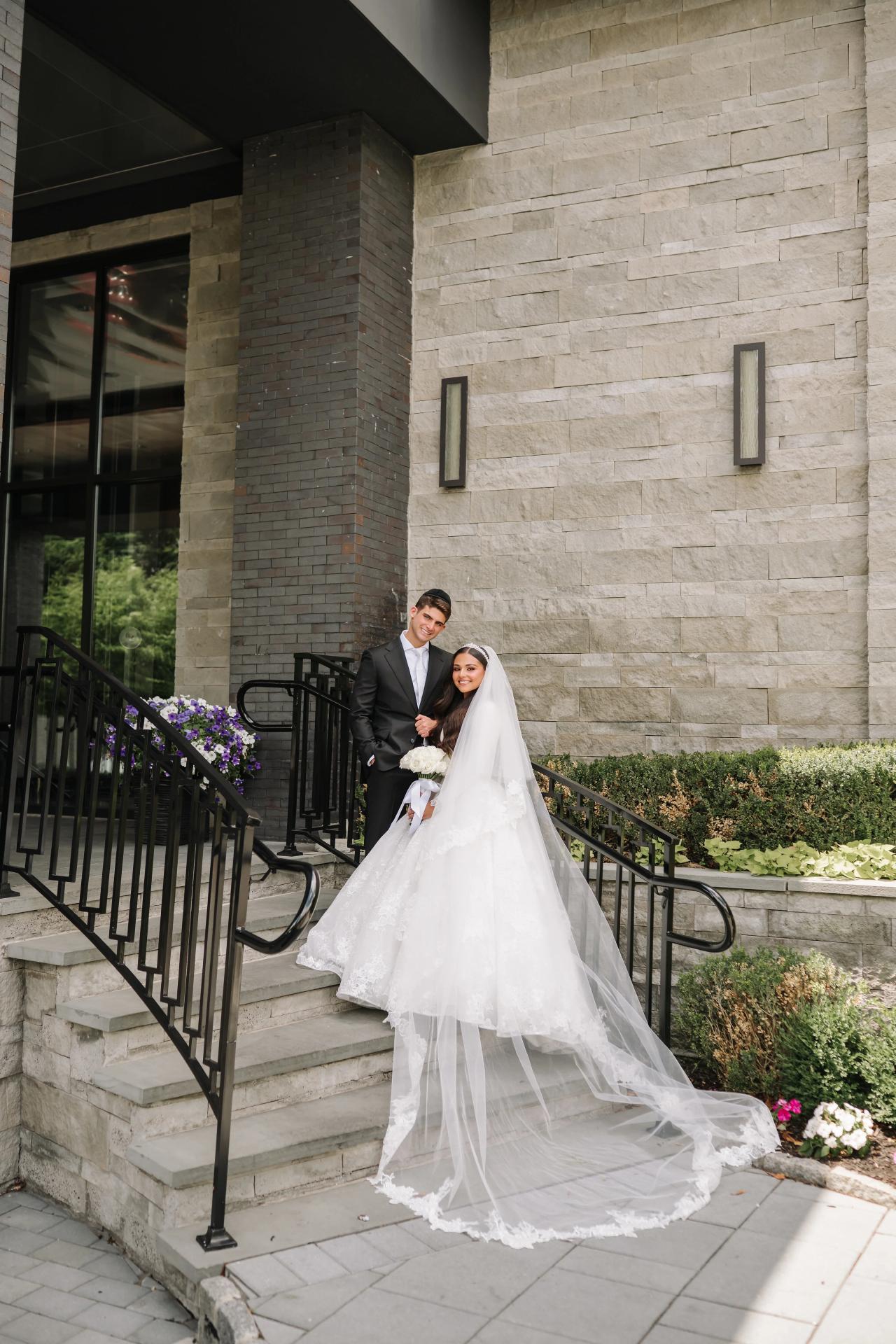 Full-length couple portrait on stone steps with a cascading lace train. Wedding photography at Brightstone, Passaic, NJ.