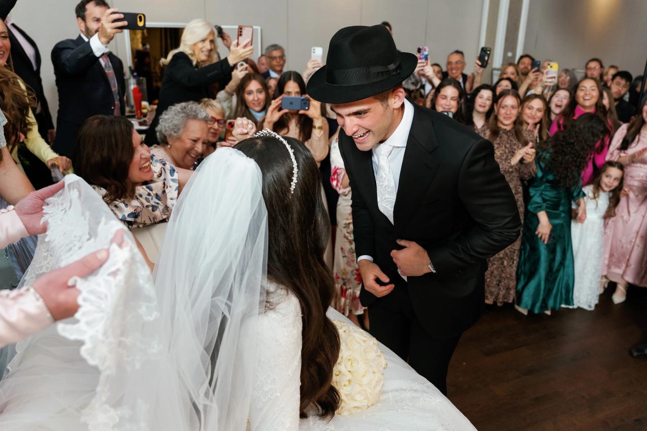 The groom reaches toward the bride during the bedeken. Wedding photography at Brightstone, Passaic, NJ.