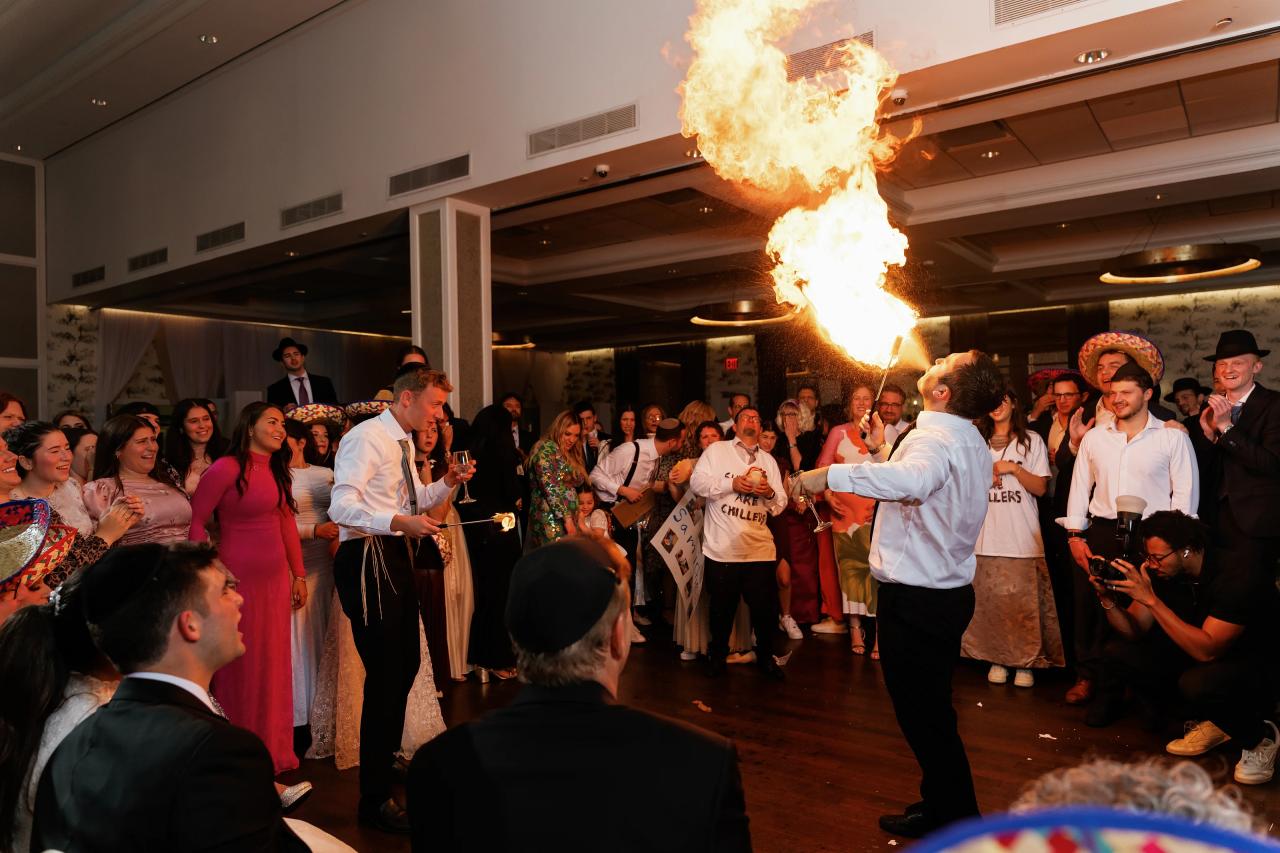 A fire-breathing performer sends a dramatic flame above a circle of wedding guests. Wedding photography at Brightstone, Passaic, NJ.