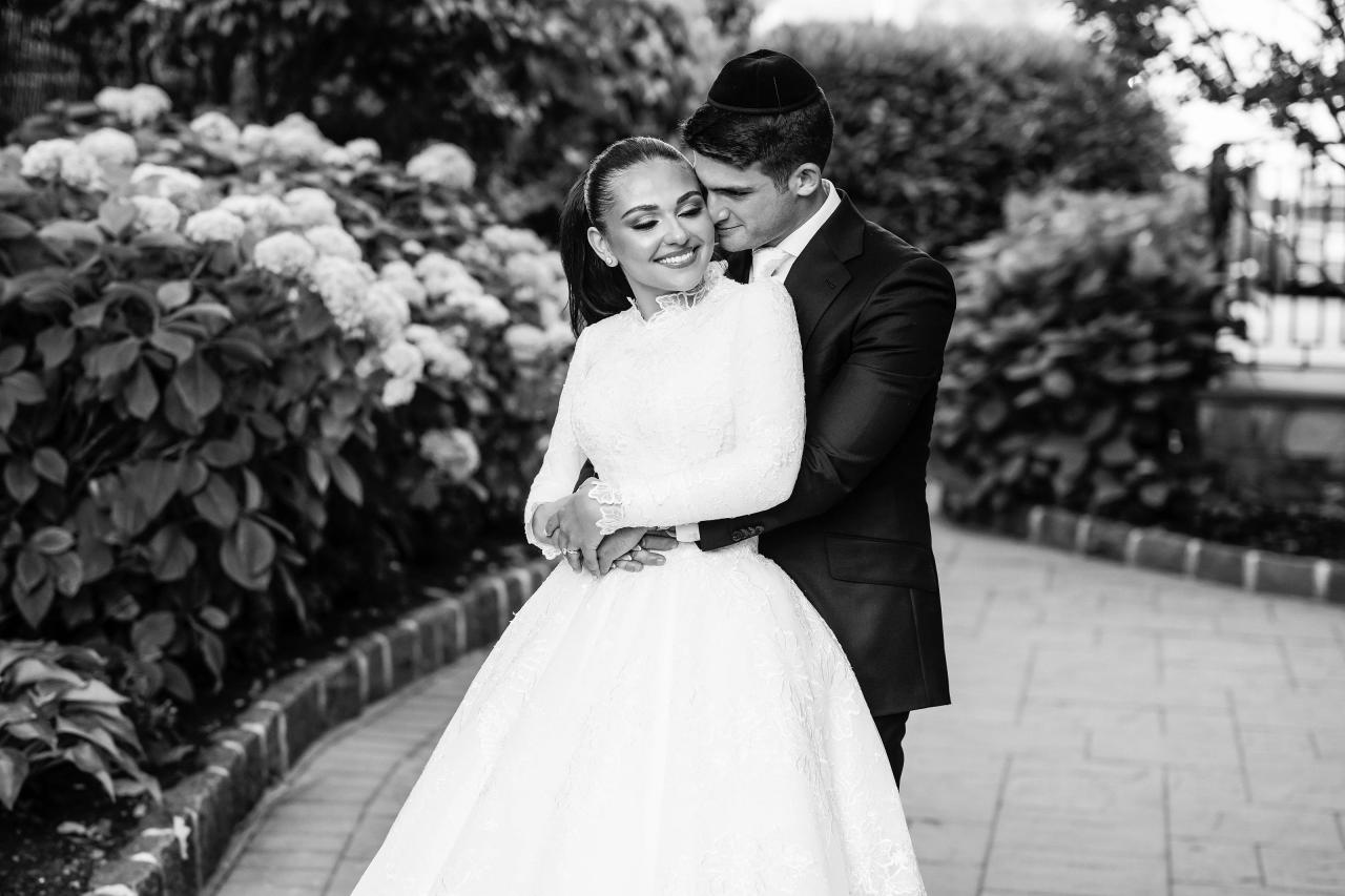 Black-and-white portrait of the couple smiling in an affectionate embrace among hydrangeas. Wedding photography at Brightstone, Passaic, NJ.