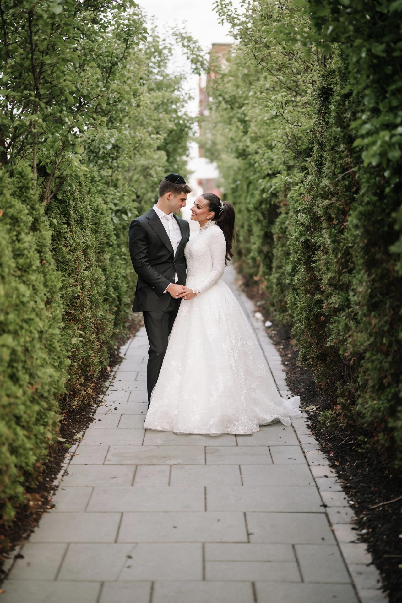 A relaxed full-length couple portrait at the end of a hedge-lined walkway. Wedding photography at Brightstone, Passaic, NJ.