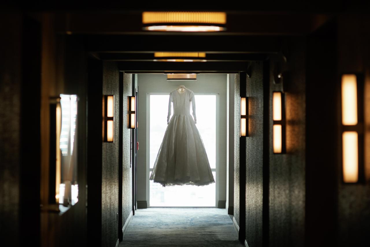 Hanging wedding dress at the end of a dark corridor; repeating ceiling lights create depth. Wedding photography at Hilton Baltimore Inner Harbor, Baltimore, MD.