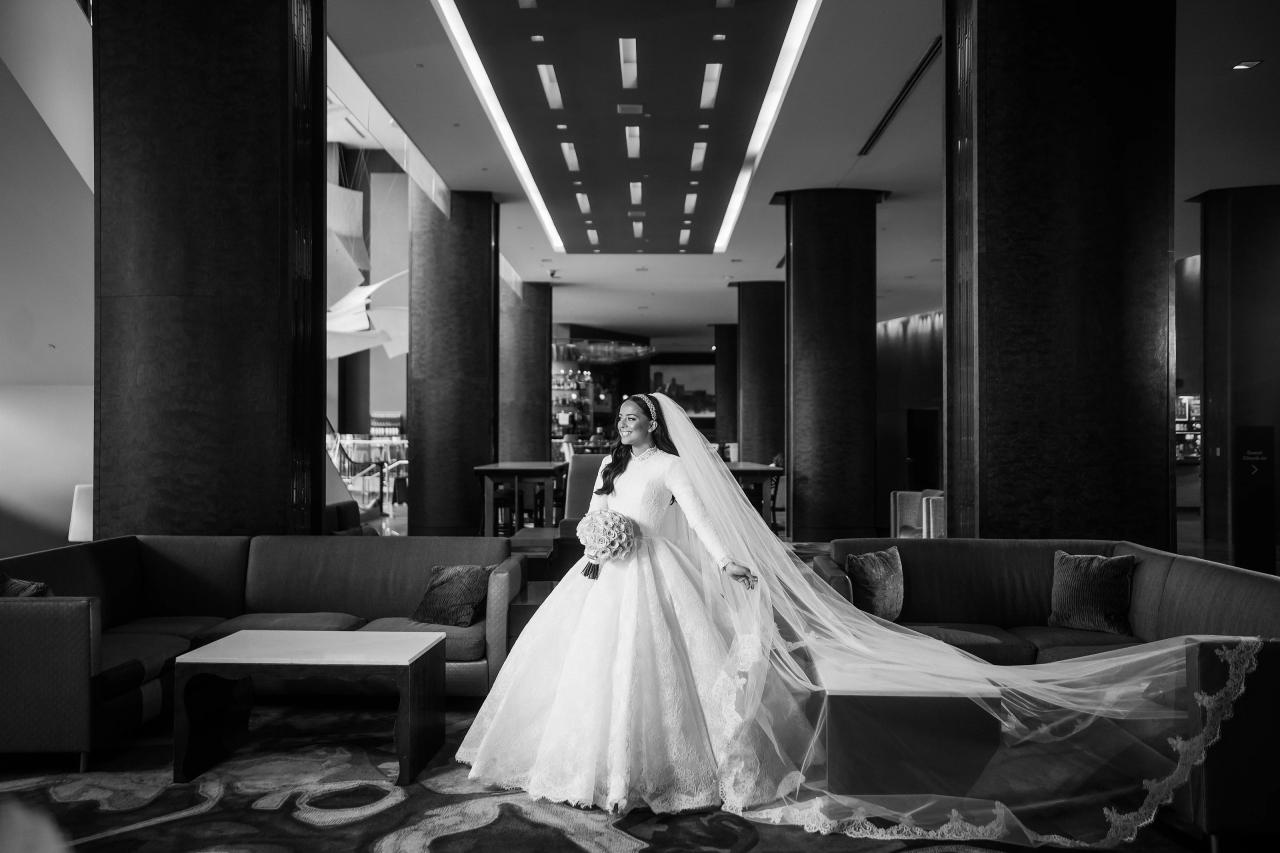 Black-and-white bridal portrait in the hotel lobby with a long veil, columns, and strong ceiling lines. Wedding photography at Hilton Baltimore Inner Harbor, Baltimore, MD.