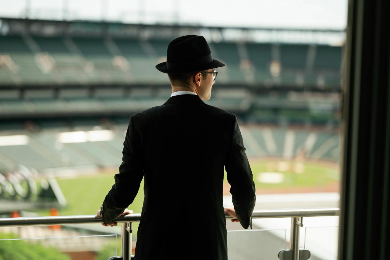 Groom looking out from the Hilton balcony over Camden Yards; distinctive location and thoughtful posture. Wedding photography at Hilton Baltimore Inner Harbor, Baltimore, MD.