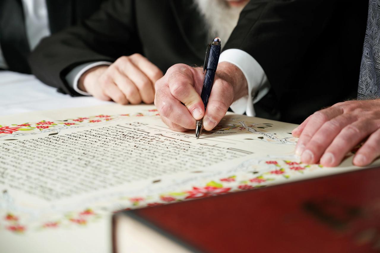 Close view of hands signing the illustrated ketubah. Wedding photography at Hilton Baltimore Inner Harbor, Baltimore, MD.