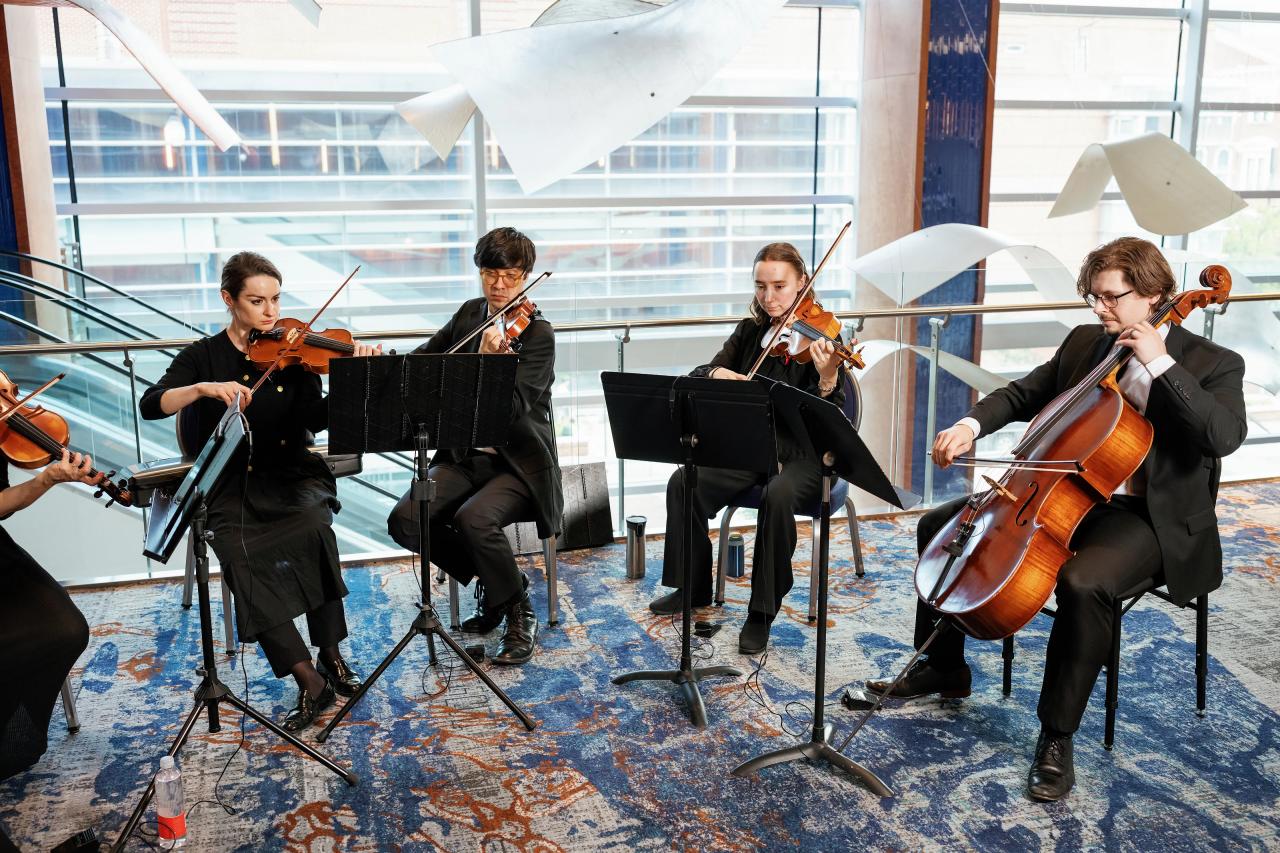 String musicians performing by the bright lobby windows and suspended sculpture. Wedding photography at Hilton Baltimore Inner Harbor, Baltimore, MD.