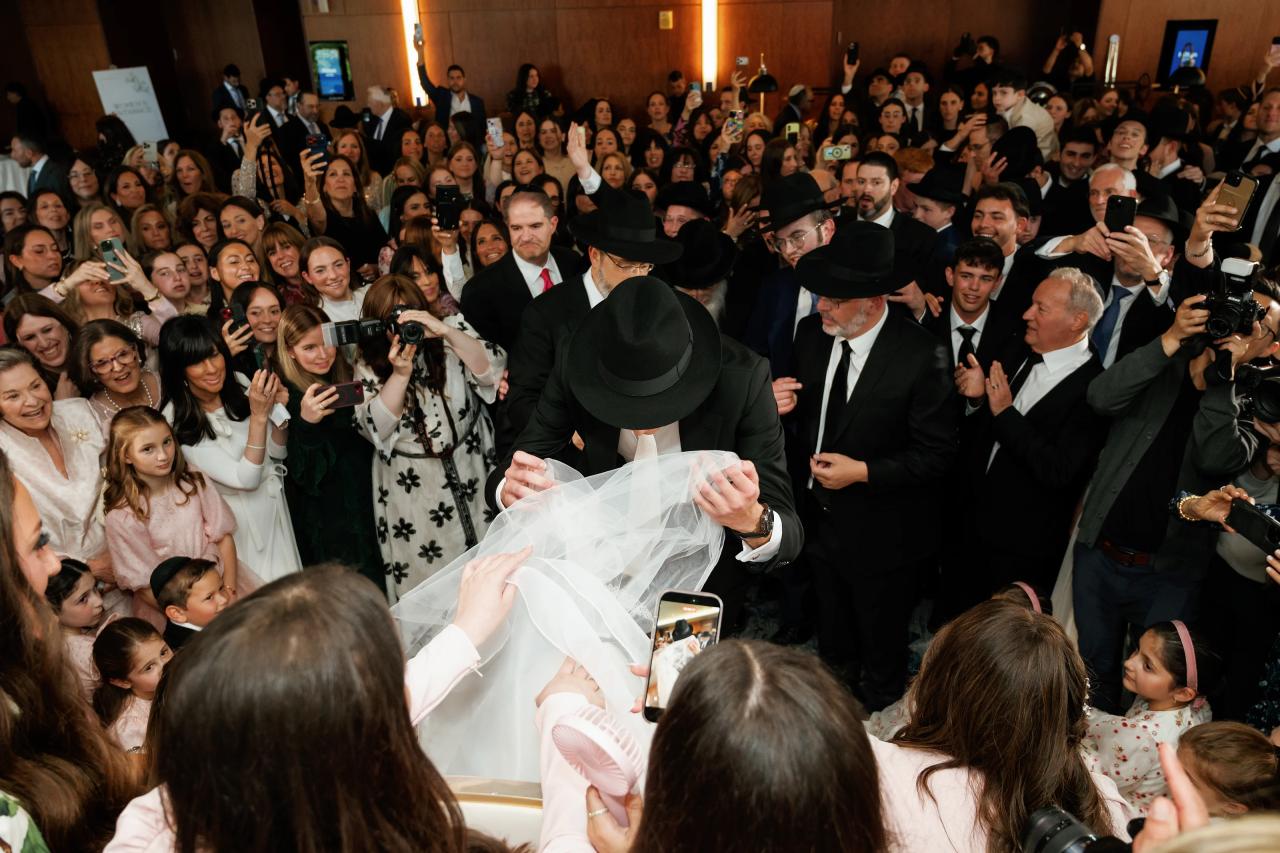 Elevated documentary view of the bedeken, with the groom drawing the veil forward and guests surrounding them. Wedding photography at Hilton Baltimore Inner Harbor, Baltimore, MD.