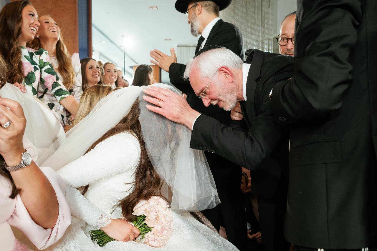 A family blessing with hands on the bride’s veiled head and guests smiling around her. Wedding photography at Hilton Baltimore Inner Harbor, Baltimore, MD.