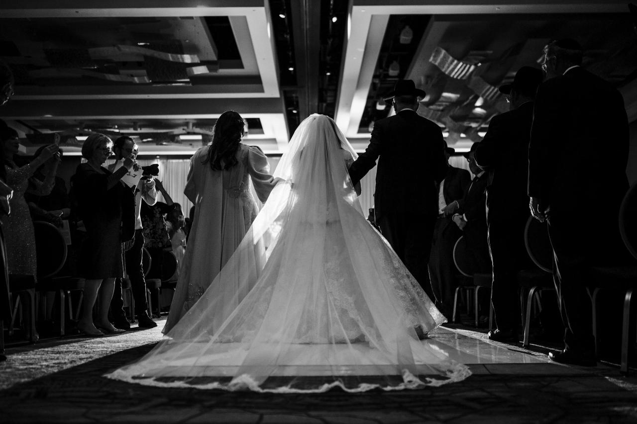 Low black-and-white view of the bride walking down the aisle, long veil emphasized by backlight. Wedding photography at Hilton Baltimore Inner Harbor, Baltimore, MD.