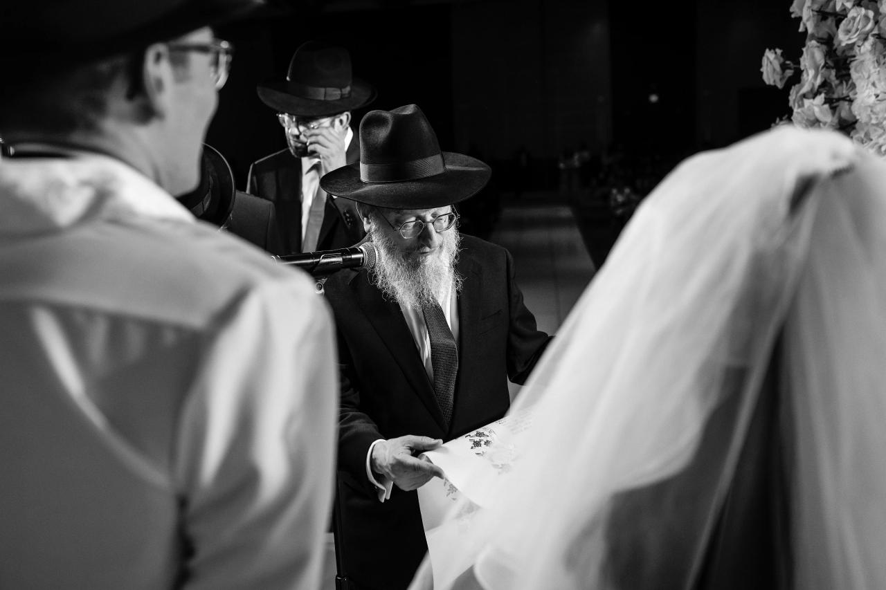 Layered black-and-white view of the rabbi between the bride and groom under the chuppah. Wedding photography at Hilton Baltimore Inner Harbor, Baltimore, MD.