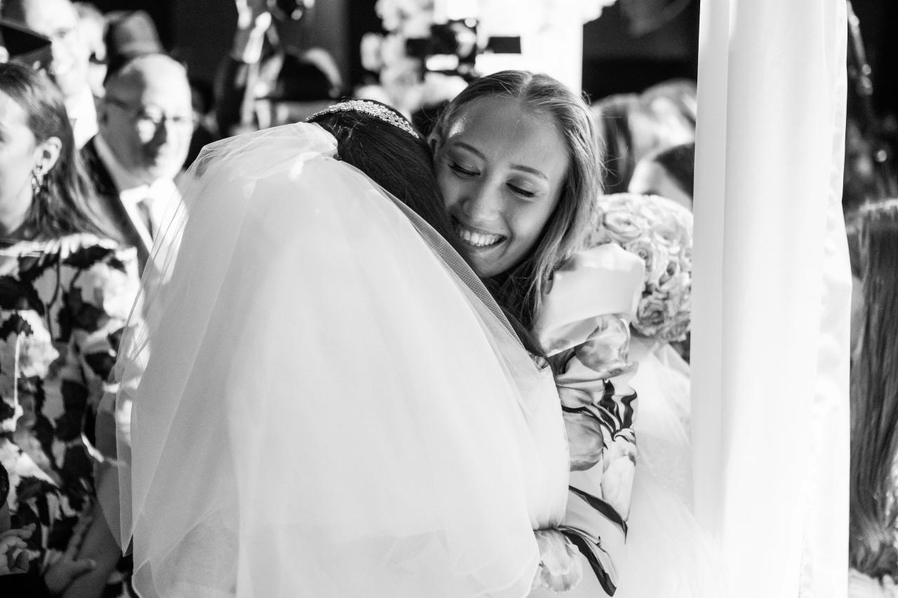 Black-and-white embrace after the chuppah, with an open smile and layered family expressions. Wedding photography at Hilton Baltimore Inner Harbor, Baltimore, MD.