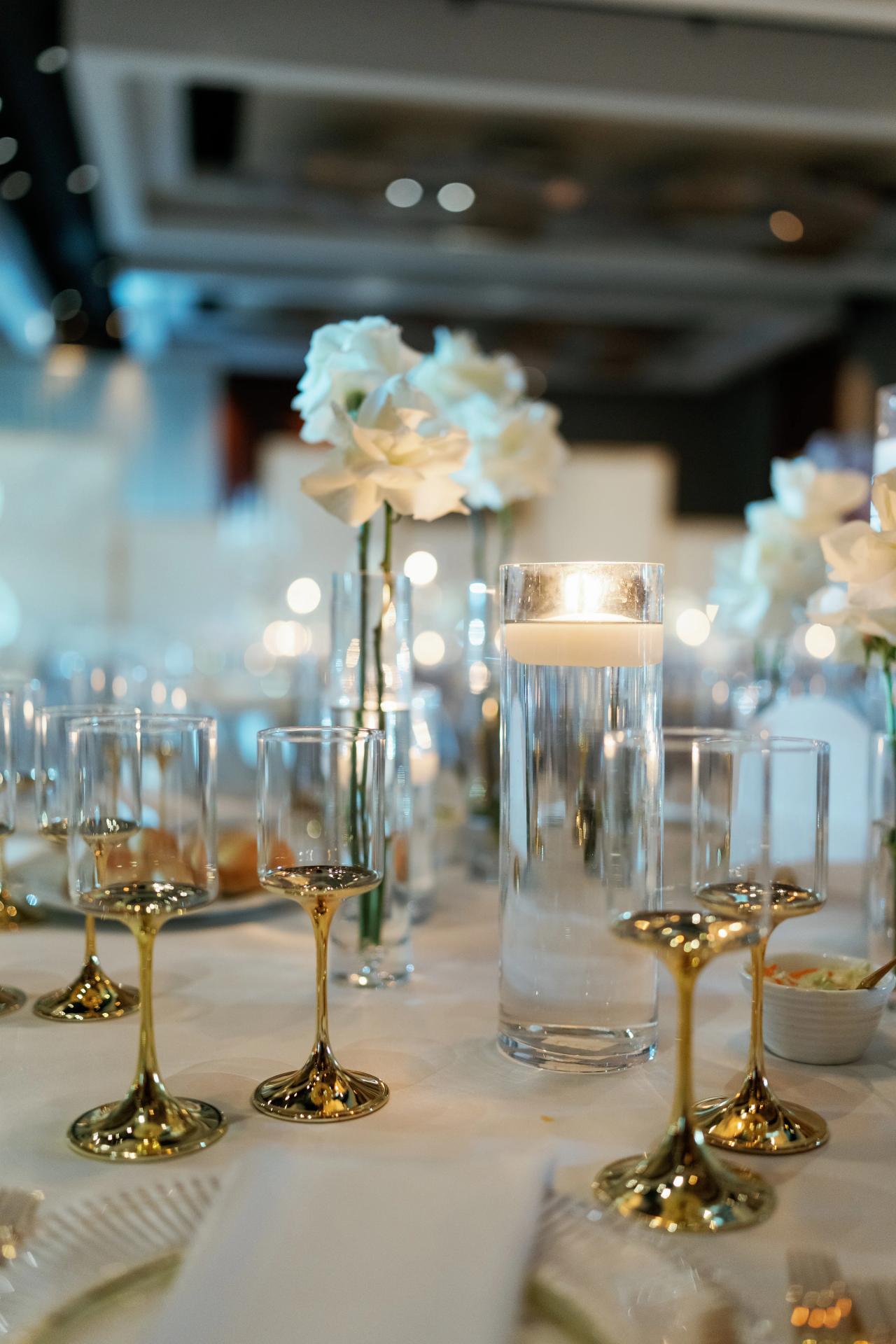 Floating candle, white rose, and gold-stemmed glasses with soft ballroom bokeh. Wedding photography at Hilton Baltimore Inner Harbor, Baltimore, MD.