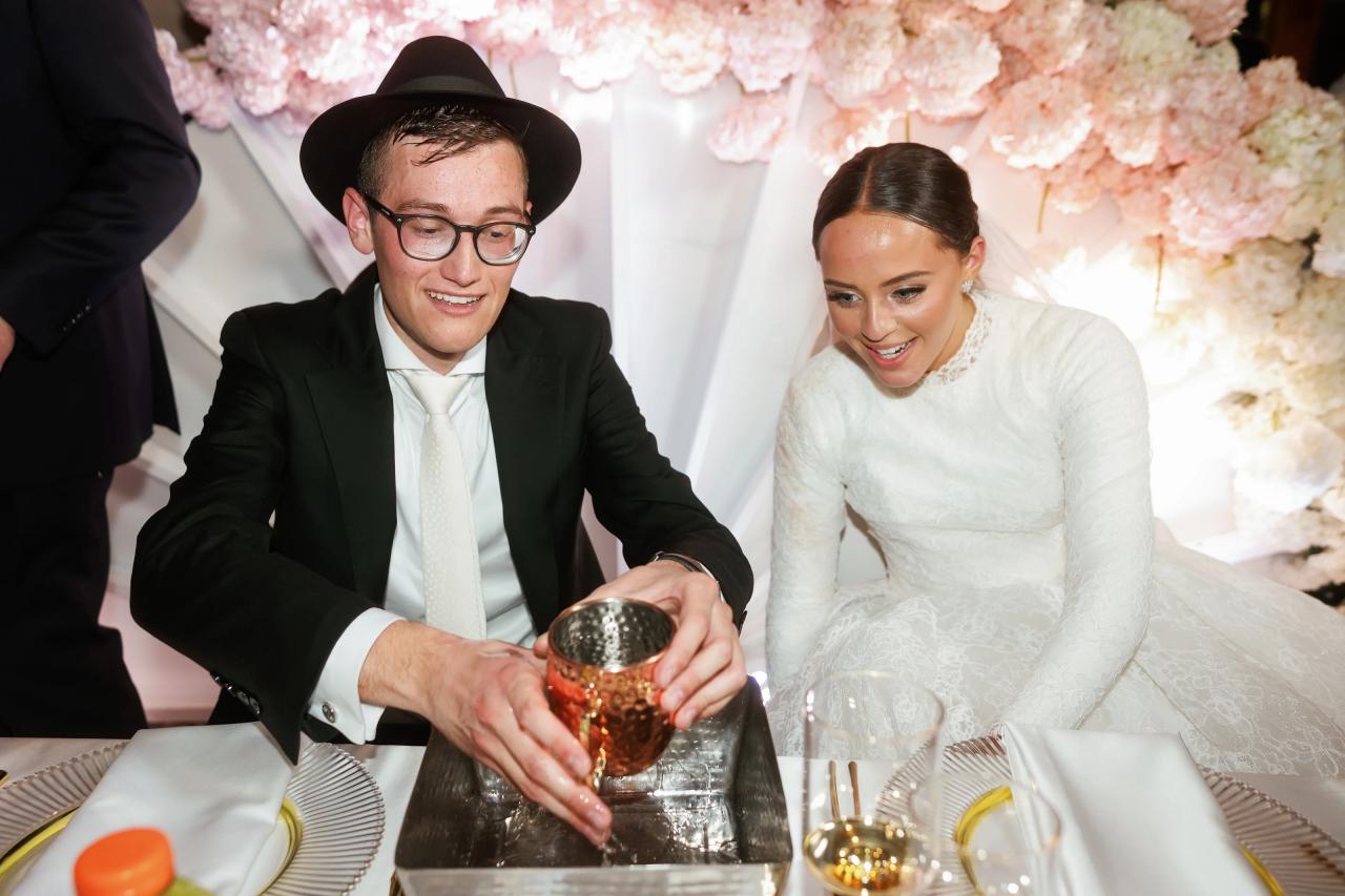 The newlyweds smiling together as the groom holds a kiddush cup at their table. Wedding photography at Hilton Baltimore Inner Harbor, Baltimore, MD.
