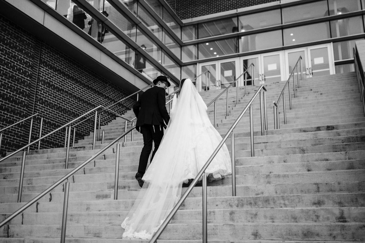 Black-and-white couple walking up a broad outdoor stairway; converging rails and trailing veil — couple portraits for the Hilton Baltimore Inner Harbor wedding. Wedding photography.