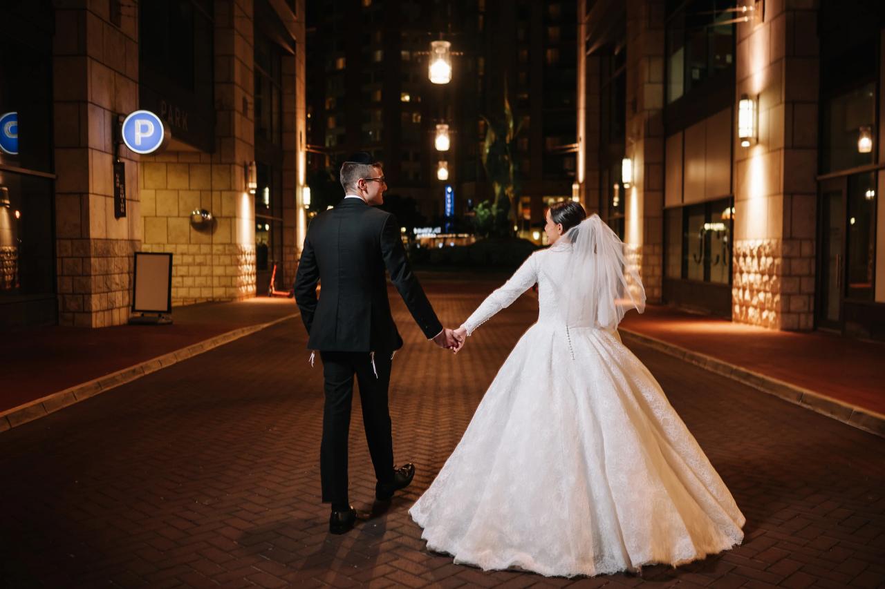 The couple looking back while walking hand in hand through a warmly lit city passage after dark — couple portraits for the Hilton Baltimore Inner Harbor wedding. Wedding photography.