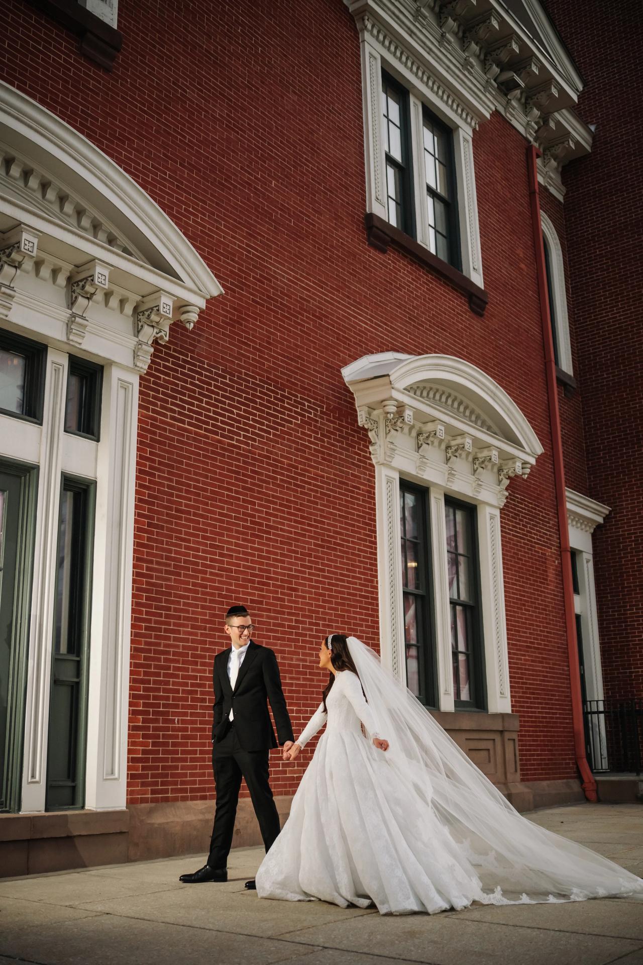 Vertical couple portrait against a red-brick historic facade, with high windows and flowing veil — couple portraits for the Hilton Baltimore Inner Harbor wedding. Wedding photography.