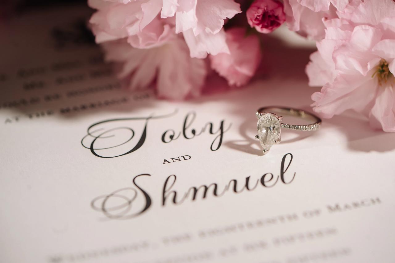 Close-up of an engagement-style ring resting on wedding invitation stationery with pink flowers in the foreground. Wedding photography at The Palace, Brooklyn, NY.
