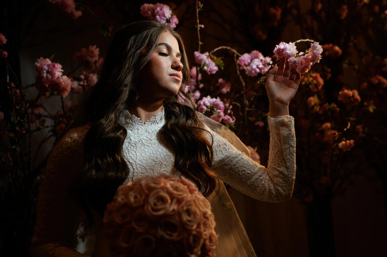 Bride with eyes closed holding pink flowers bouquet in a warm, softly lit floral backdrop. Wedding photography at The Palace, Brooklyn, NY.