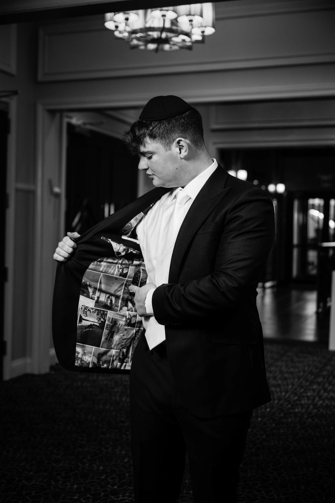 Black-and-white candid of the groom holding a photo album collage close to his chest while looking down in a quiet moment during the reception. Wedding photography at The Palace, Brooklyn, NY.