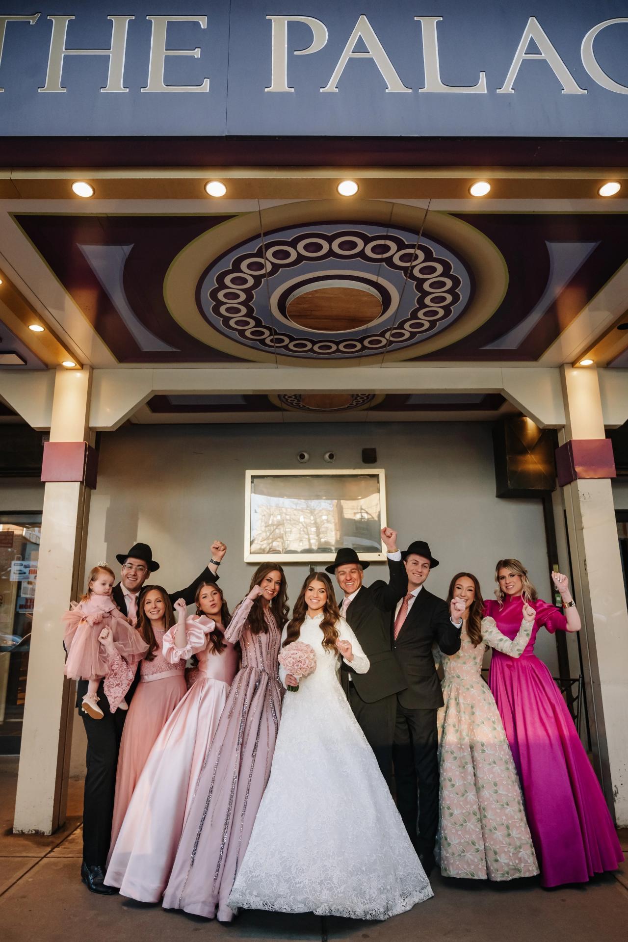 Framed group celebration at a wedding finale with the couple centered and guests around them raising hands in a reception hall entrance. Wedding photography at The Palace, Brooklyn, NY.