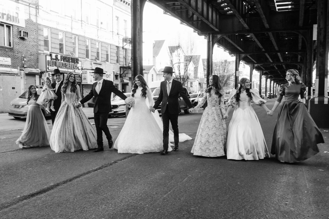 Black-and-white street exit photo with a bride and groom walking forward while guests run and celebrate on both sides under a canopy. Wedding photography at The Palace, Brooklyn, NY.