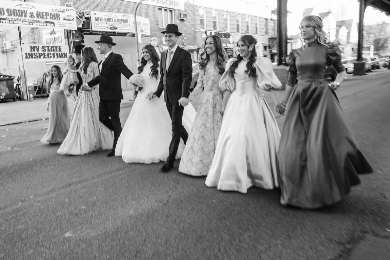 Black-and-white candid of a wedding bridal party walking outdoors on a city sidewalk, skirts flowing and people laughing mid-motion. Wedding photography at The Palace, Brooklyn, NY.