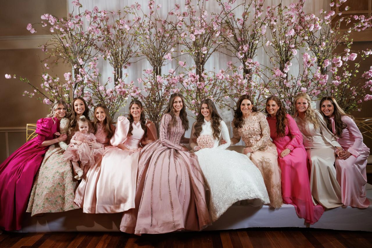 Smiling family seated on a stage in front of a large pink floral tree backdrop during a celebration. Wedding photography at The Palace, Brooklyn, NY.