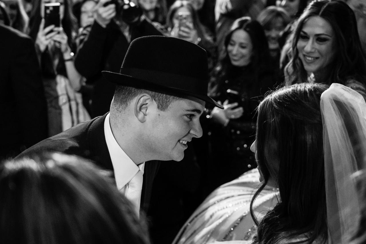 Black-and-white close-up of a groom and bride laughing during the reception, with confetti and guests in the background. Wedding photography at The Palace, Brooklyn, NY.