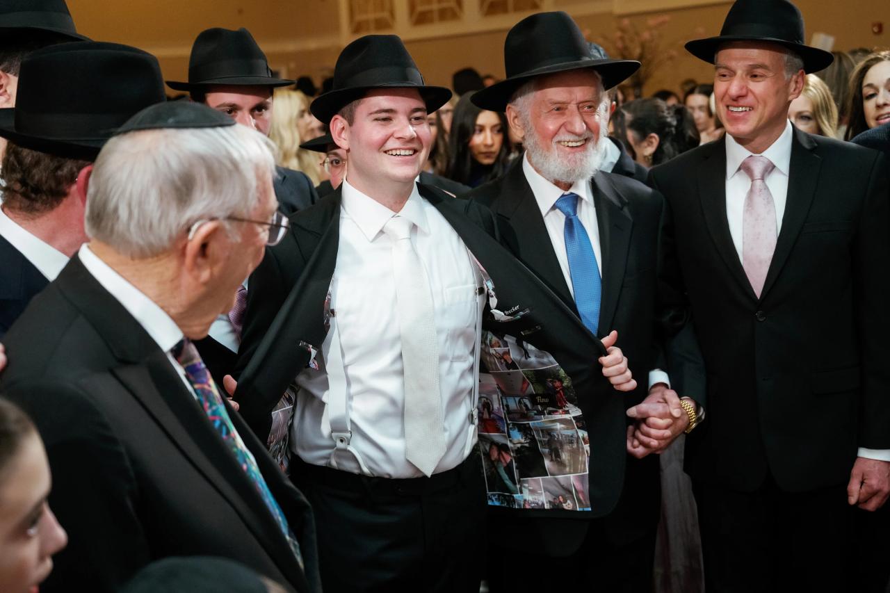 Close candid of a group of men in formal attire and hats smiling and conversing at an indoor celebration. Wedding photography at The Palace, Brooklyn, NY.