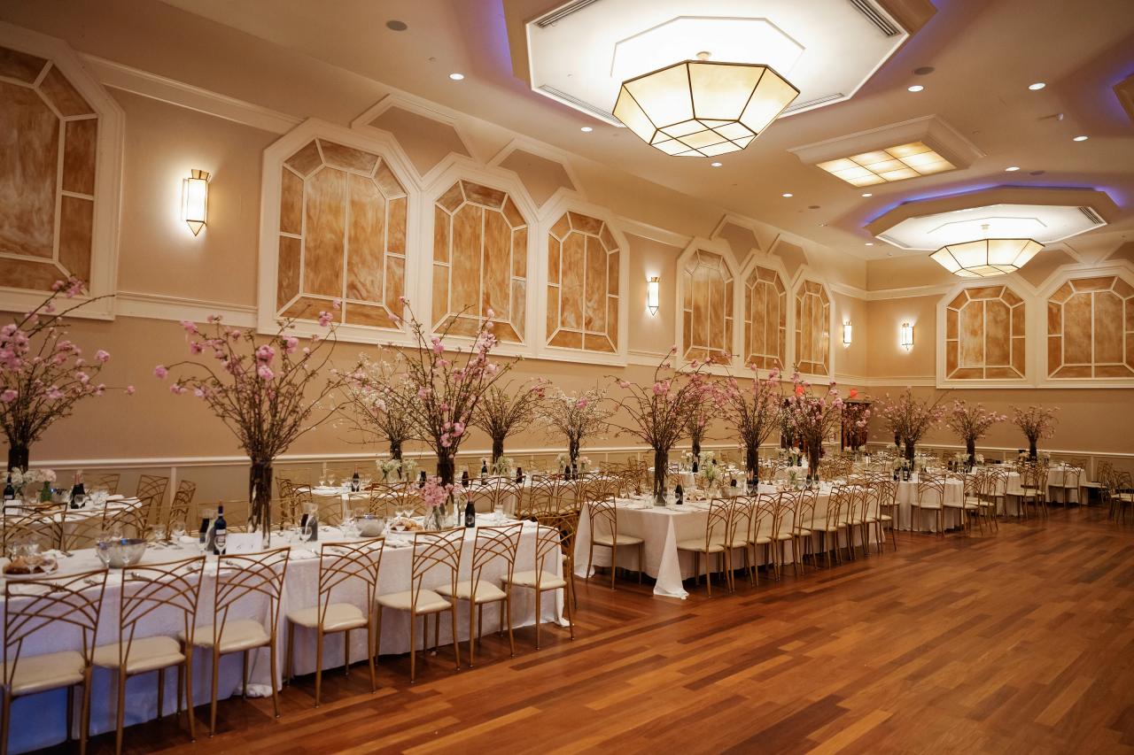 Wide view of a decorated reception ballroom with banquet tables, gold chairs, and pink blossom trees in bloom. Wedding photography at The Palace, Brooklyn, NY.