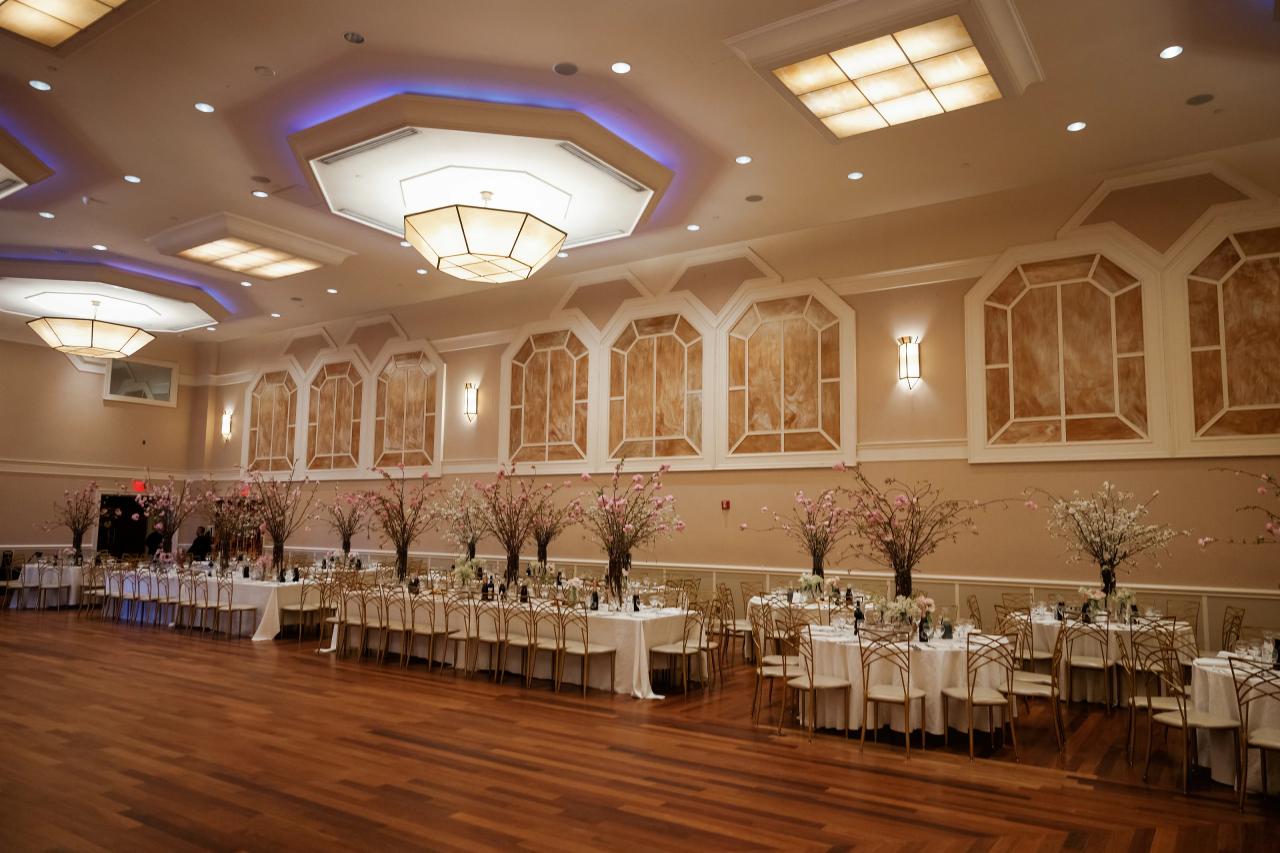 Wide view of a reception ballroom with set tables, chairs, floral tree centerpieces along the walls, and warm overhead lighting. Wedding photography at The Palace, Brooklyn, NY.