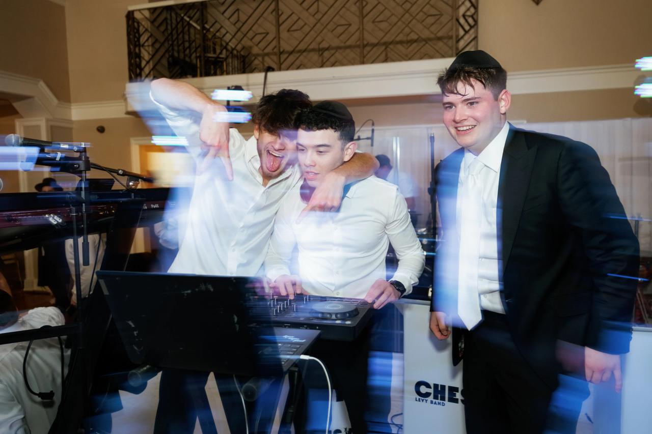 Smiling groom laughing closely with friends at the DJ booth during reception dancing, with blue light trails and motion in the scene. Wedding photography at The Palace, Brooklyn, NY.