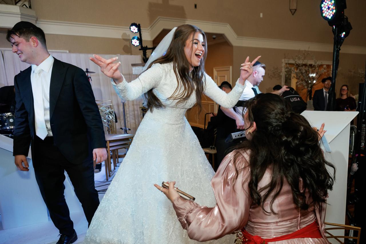 Bride laughing with arms raised on the dance floor as guests cheer closely beside her at a wedding reception. Wedding photography at The Palace, Brooklyn, NY.