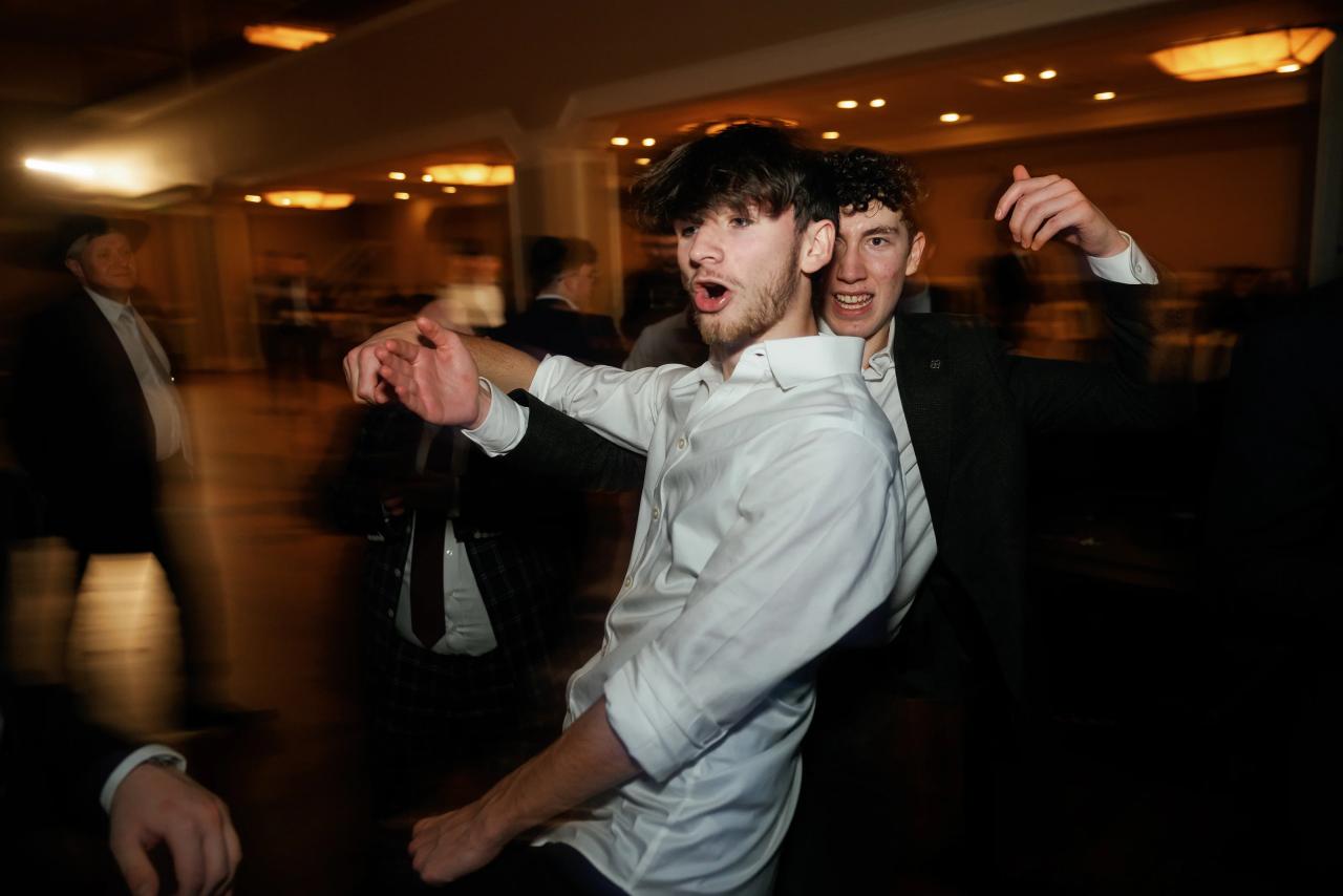 Smiling groom in a white shirt dancing at a wedding reception with a friend in the background, captured with intentional motion blur and warm indoor lighting. Wedding photography at The Palace, Brooklyn, NY.