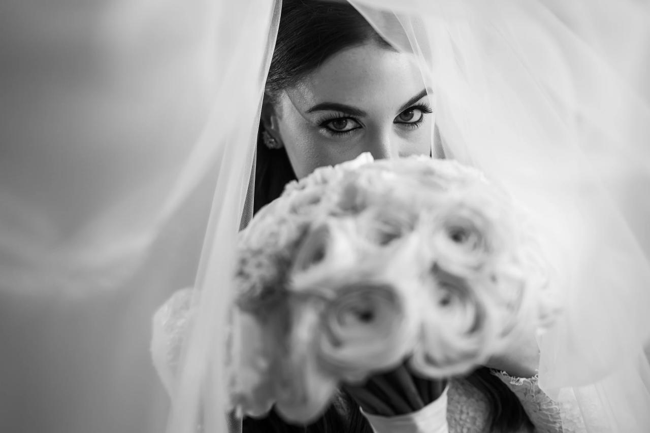Black-and-white portrait of the bride looking over a softly blurred rose bouquet beneath her veil. From this Lake Terrace wedding. Wedding photography.