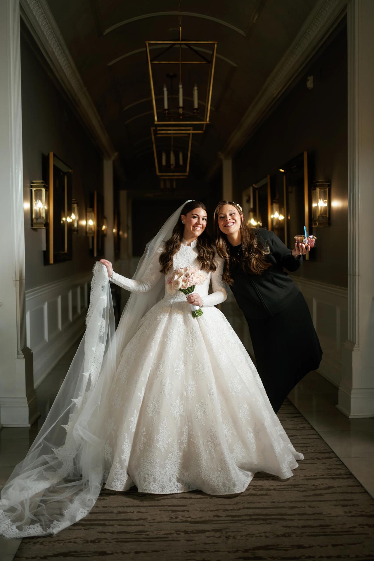 The bride and a woman in black smile together in a long, lantern-lit corridor. From this Lake Terrace wedding. Wedding photography.