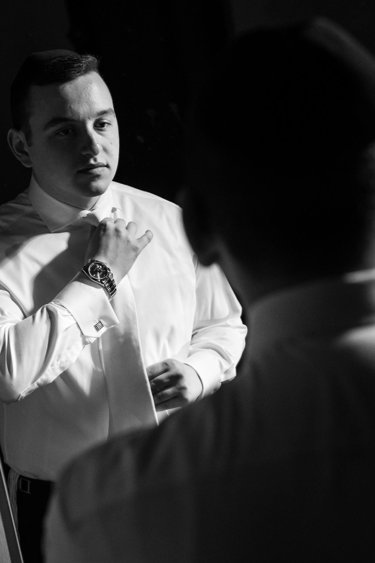 Black-and-white reflection of the groom adjusting his white tie during preparations. From this Lake Terrace wedding. Wedding photography.