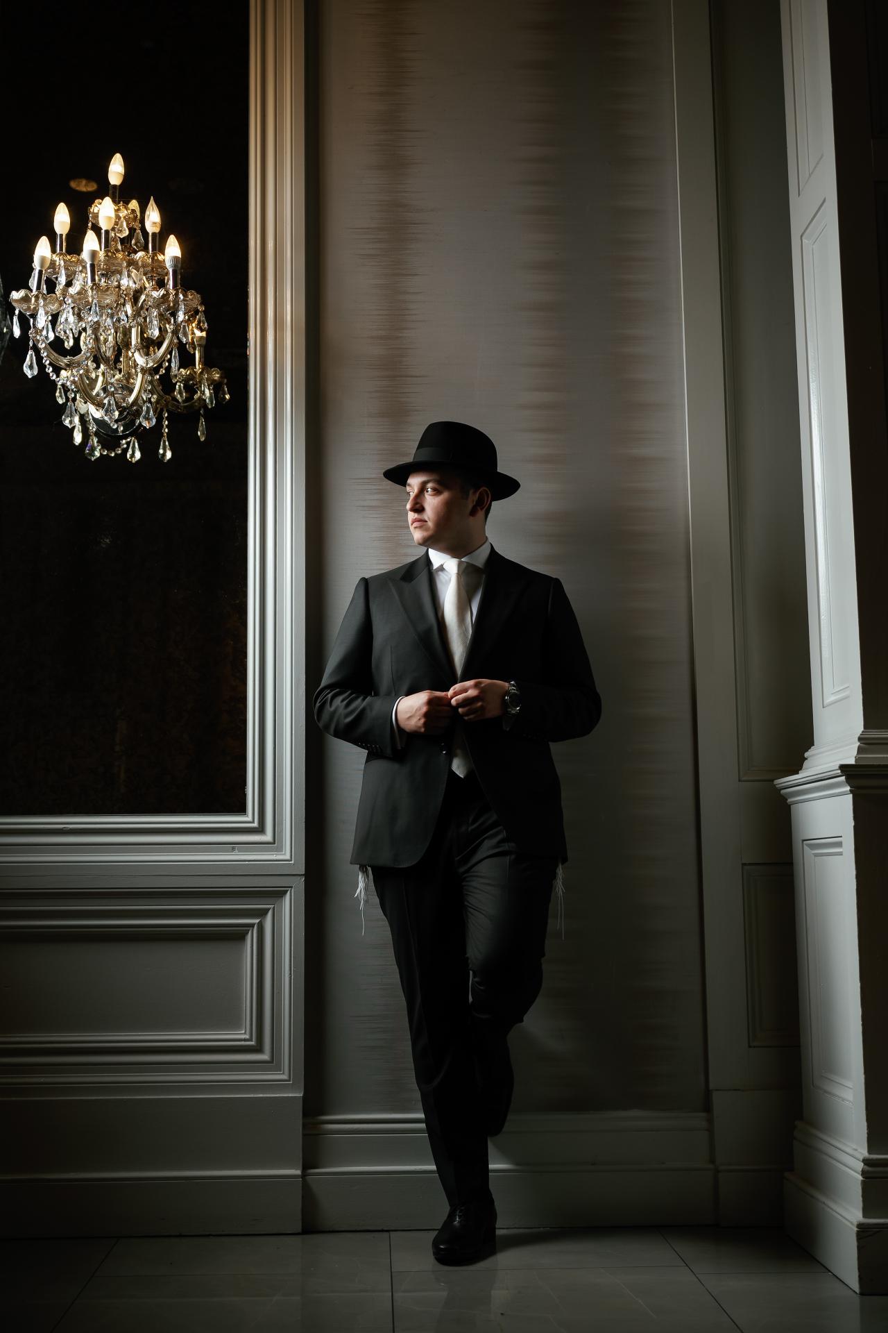 The groom stands in a paneled doorway beside a glowing crystal wall light. From this Lake Terrace wedding. Wedding photography.