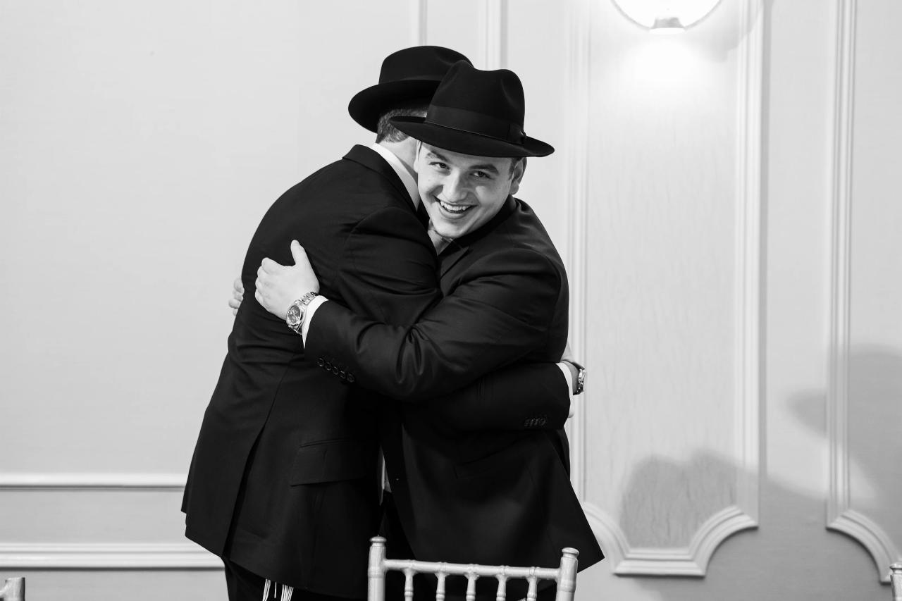 Black-and-white photograph of the smiling groom embracing another man before the ceremony. From this Lake Terrace wedding. Wedding photography.