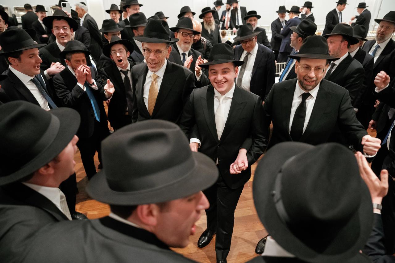 The smiling groom walks hand in hand with men through a crowd of singing guests. From this Lake Terrace wedding. Wedding photography.