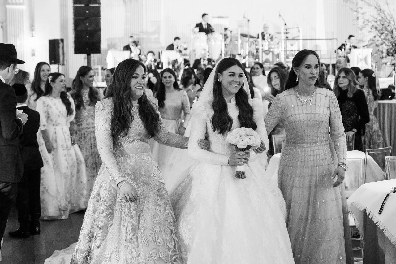 Black-and-white photograph of the bride walking arm in arm with two women as guests follow. From this Lake Terrace wedding. Wedding photography.