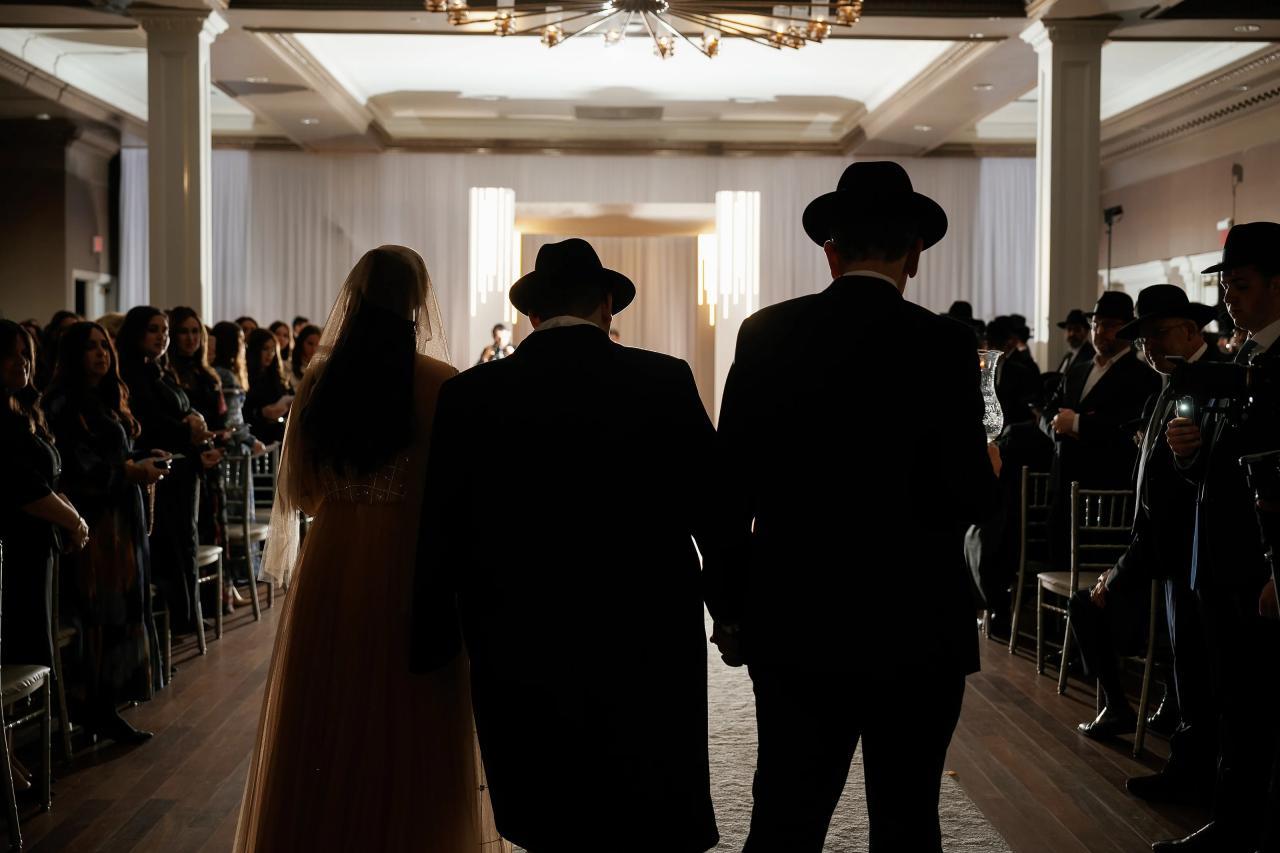 Backlit view of the groom entering the ceremony aisle with family. Wedding photography at Lake Terrace, Lakewood, NJ.
