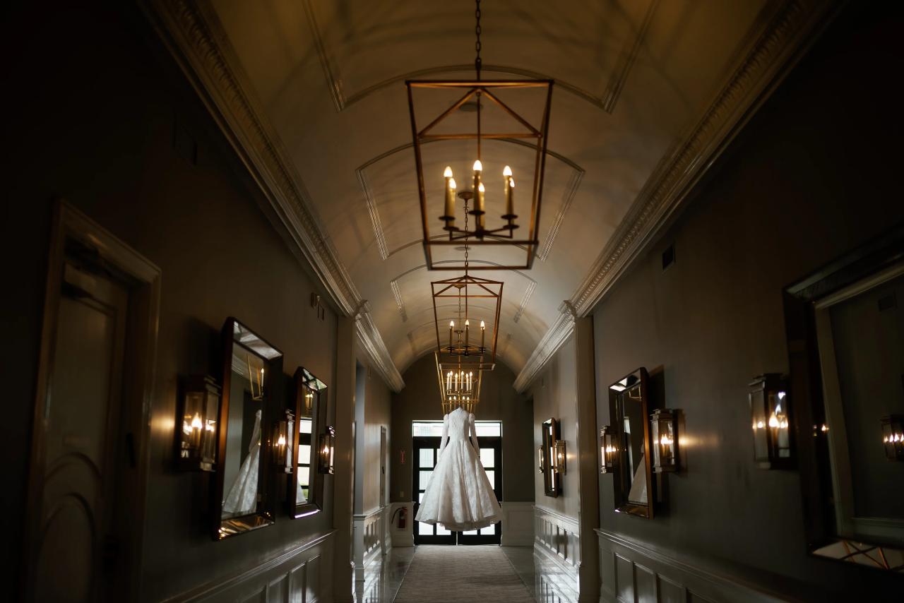 A wedding gown hanging at the end of a lantern-lit hallway, from the Lake Terrace wedding in Lakewood, New Jersey.