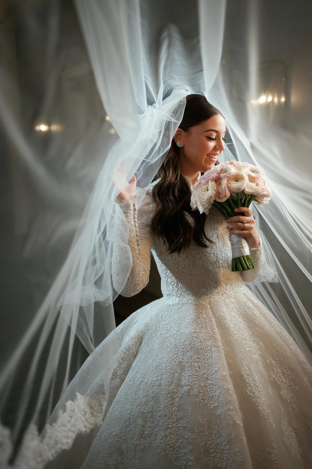 Framed bridal portrait with a soft veil arc and warm light, the bride smiling while holding a bouquet. Wedding photography at Lake Terrace, Lakewood, NJ.