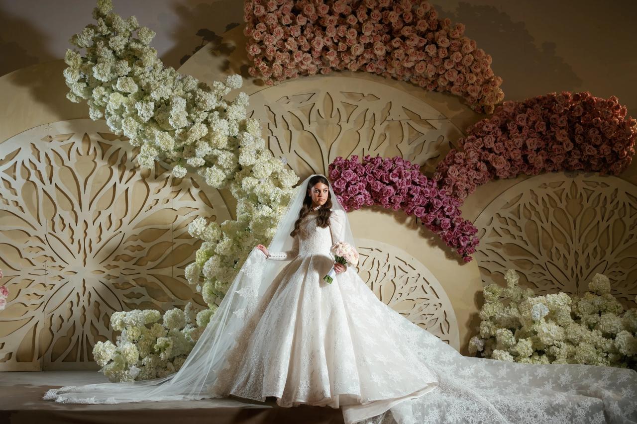 Framed bridal portrait of a girl in a white dress and veil standing centered before a large floral wall, holding a bouquet on a decorated stage. Wedding photography at Lake Terrace, Lakewood, NJ.