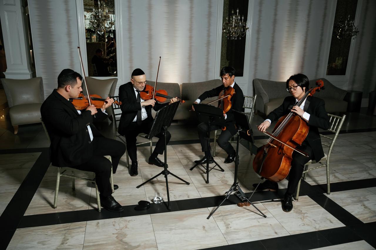 A seated string quartet performing with violins and cello in a formal hall with white columns and music stands. Wedding photography at Lake Terrace, Lakewood, NJ.