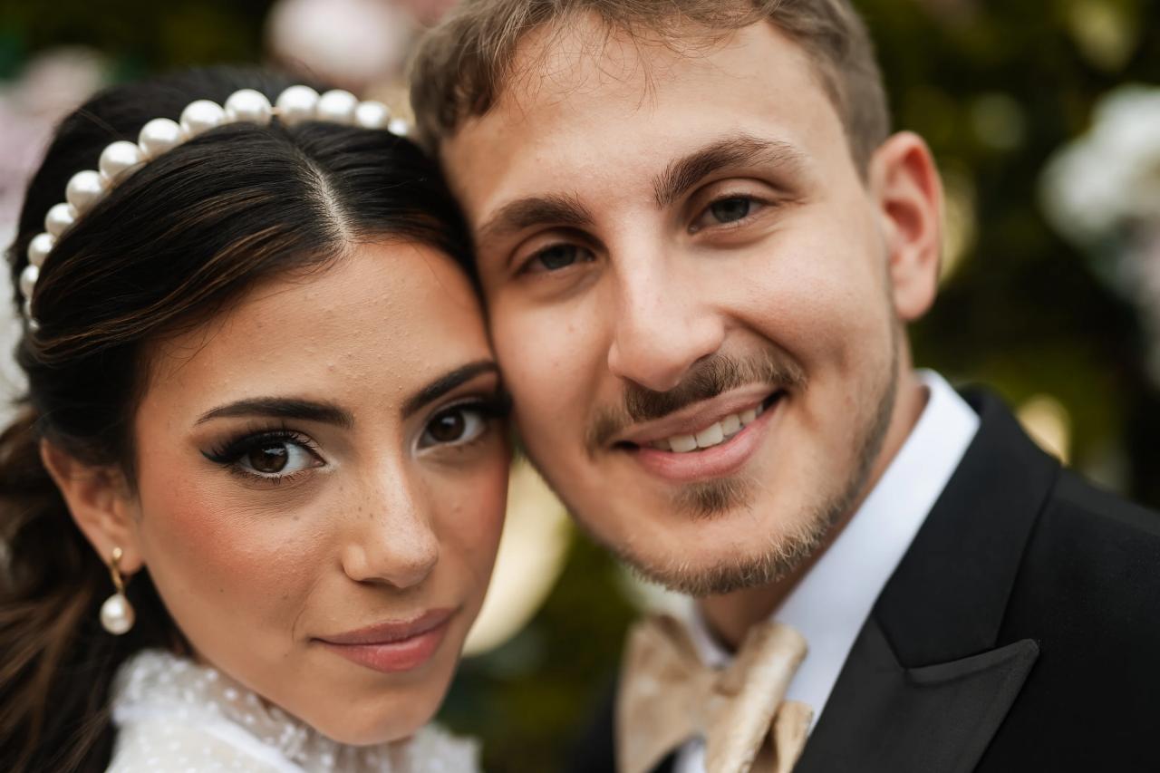 Close-up wedding portrait of a smiling couple leaning together, with the bride wearing a pearl headband.