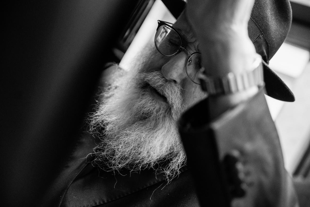 Intimate black-and-white close-up of an elder’s face during a pre-ceremony blessing, framed closely by raised arms. From this Oholei Torah Ballroom wedding. Wedding photography.
