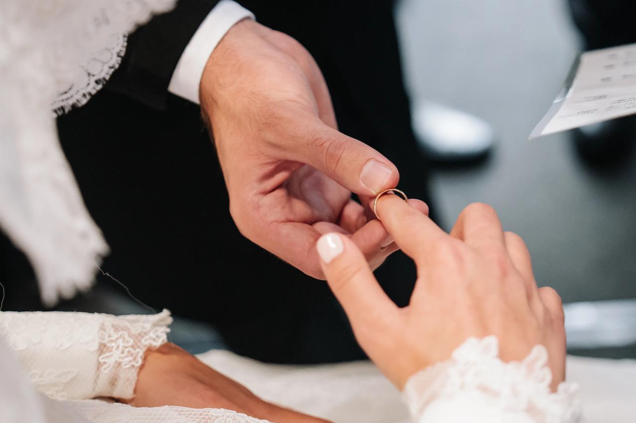 Close-up of the groom placing a gold wedding ring on the bride's finger during the chuppah. From this Oholei Torah Ballroom wedding. Wedding photography.