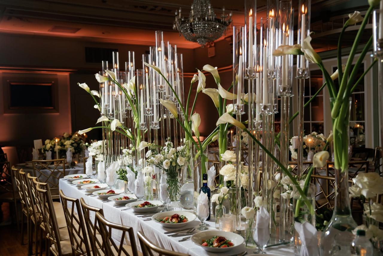 Tall taper candles in clear glass cylinders and white calla lilies line a wedding reception table. From this Oholei Torah Ballroom wedding. Wedding photography.
